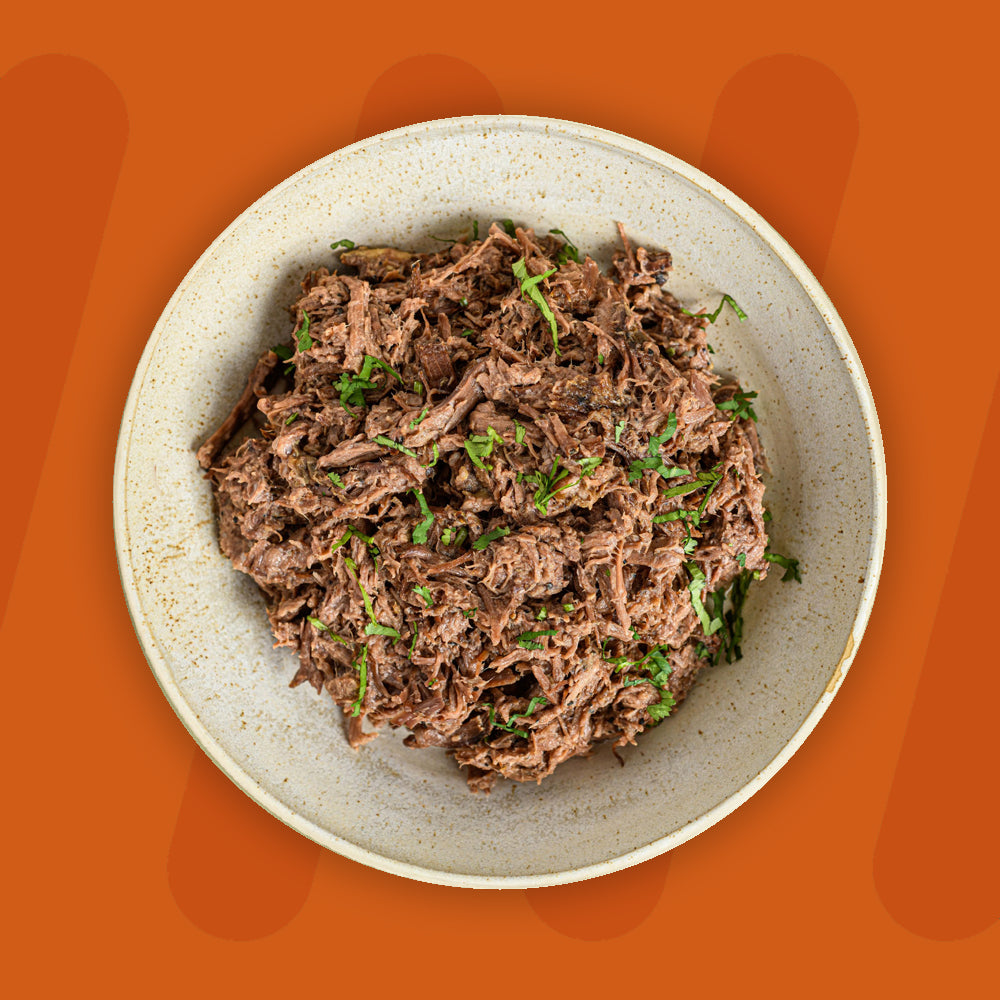 A bowl of tender shredded beef garnished with fresh herbs, set against a vibrant orange background