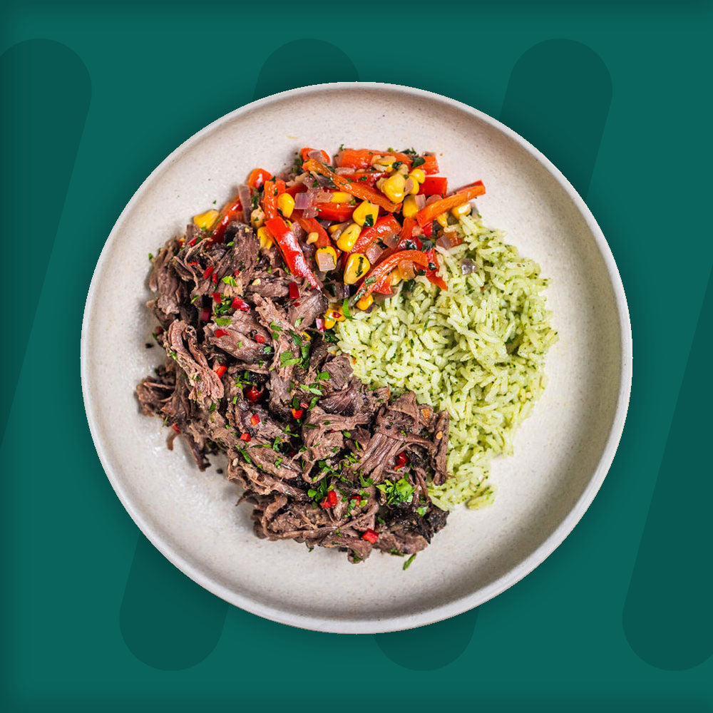 A plate of shredded beef garnished with herbs, served alongside green herb rice and a colorful medley of sautéed peppers and corn, set against a teal background