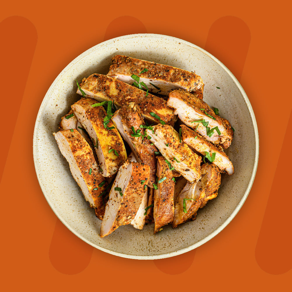 "A bowl filled with slices of seasoned grilled chicken, garnished with fresh herbs, displayed against a bright orange background