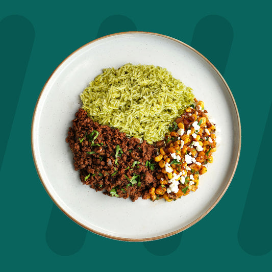 A plated meal featuring green herb rice, seasoned ground beef garnished with fresh herbs, and roasted corn with crumbled feta cheese, set against a teal background