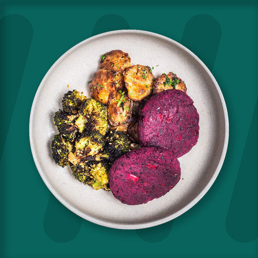 This vibrant dish features nutrient-rich beetroot patties, offering a hearty and earthy flavor, complemented by golden smashed potatoes, roasted with herbs to enhance their crispiness and soft interior. On the side, roasted broccoli florets are charred to perfection, sprinkled with toasted garlic slices for an added burst of flavor. The minimalist presentation on a beige plate against a deep green backdrop creates a visually appealing and healthy meal
