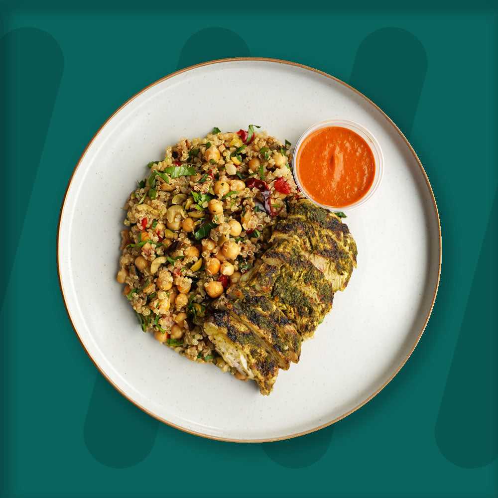 prepped meal, A nutritious plate featuring grilled herb-marinated chicken breast slices, paired with a refreshing quinoa and chickpea salad tossed with fresh herbs and colorful vegetables. Accompanying the dish is a vibrant red pepper sauce served in a small container. The meal is beautifully presented on a light ceramic plate with a dark rim, set against a deep green background that enhances its fresh and wholesome appeal