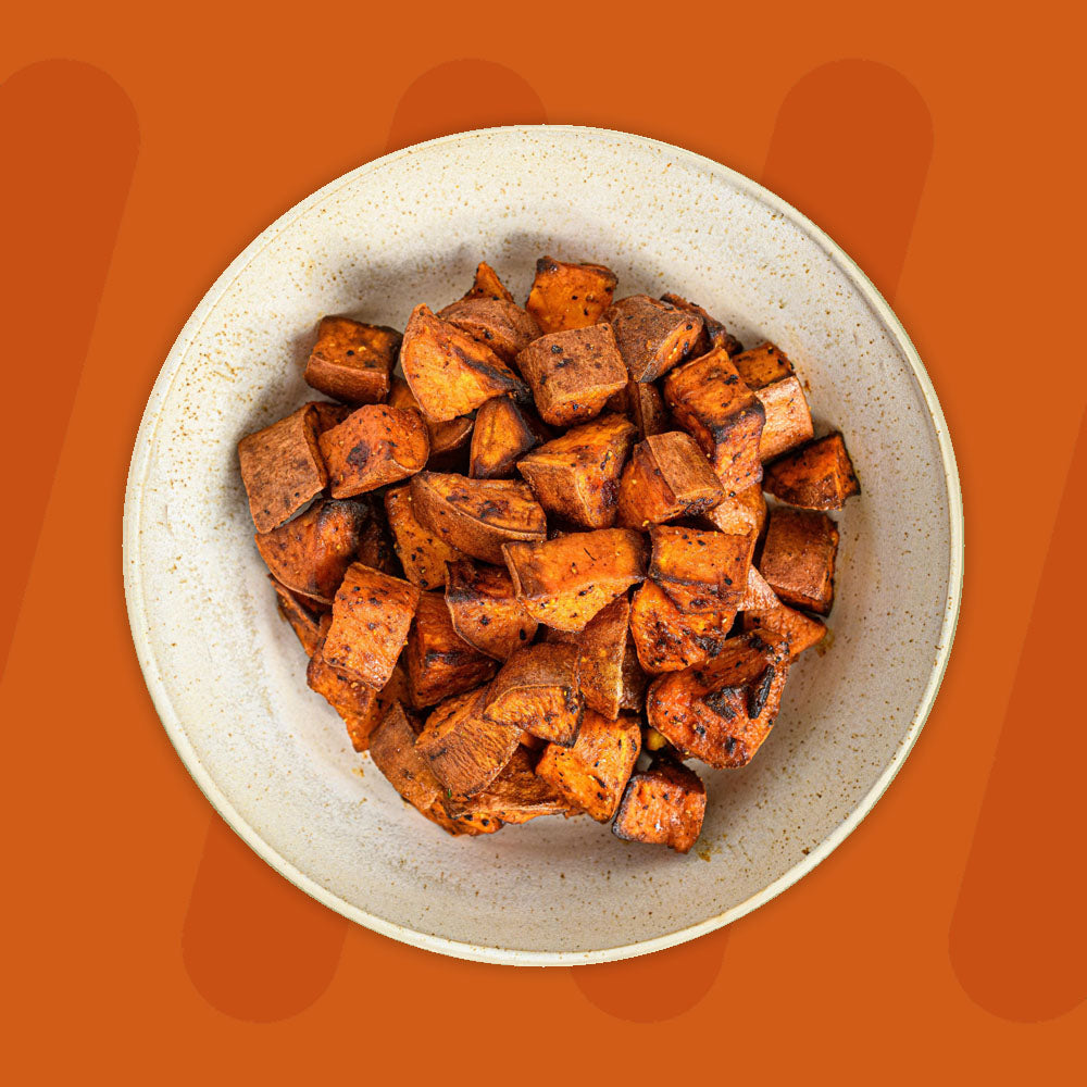 A bowl of roasted sweet potato cubes, golden brown and seasoned to perfection, displayed against a warm orange background.