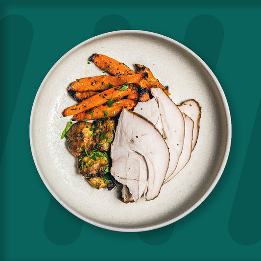 prepped meal, A wholesome meal featuring tender slices of roasted turkey, accompanied by herb-crusted smashed potatoes and roasted carrots seasoned with fresh parsley. The dish is served in a simple ceramic bowl, set against a dark green background that enhances the earthy and vibrant tones of the meal.